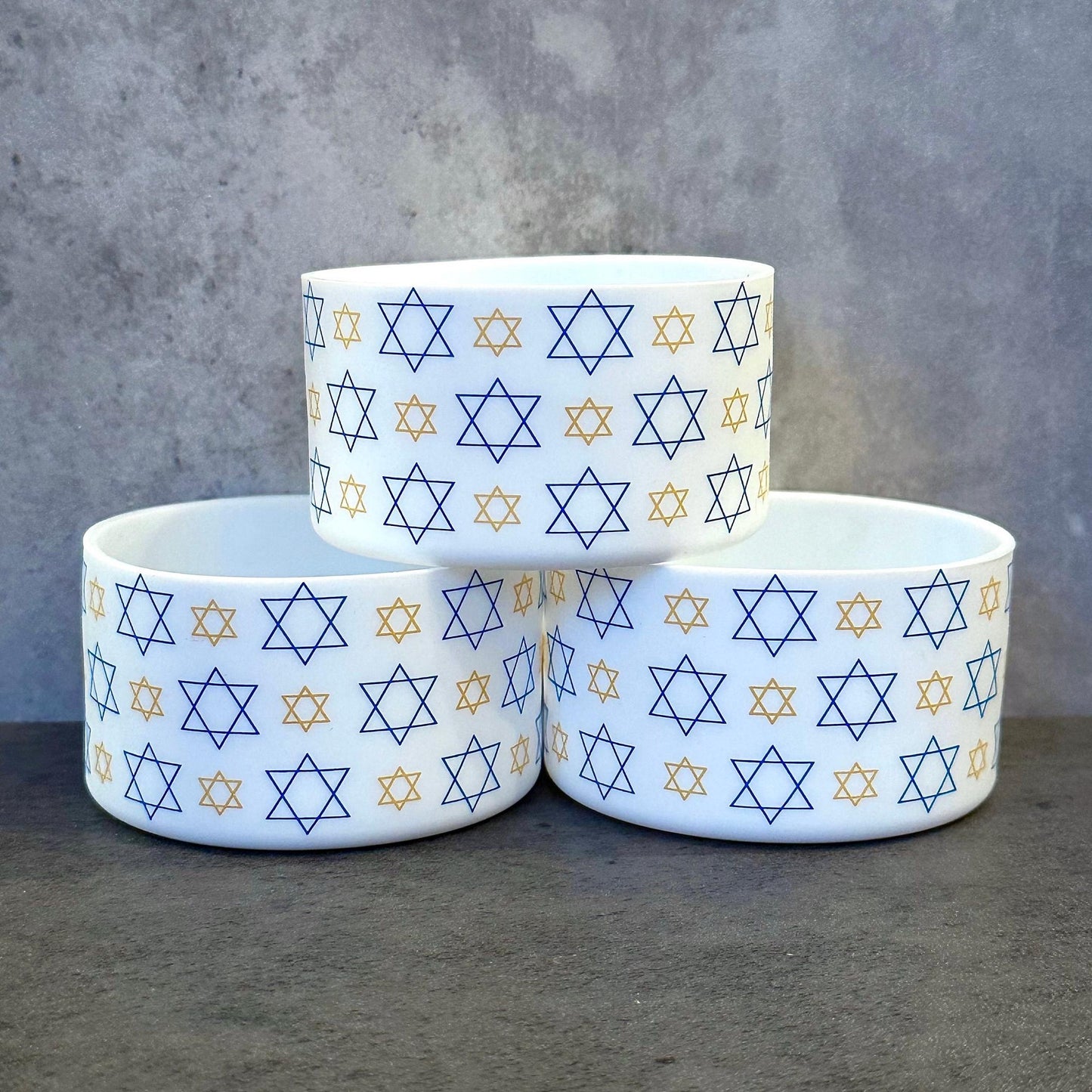 May include: Three white ceramic bowls with a blue and gold star of David pattern. The bowls are stacked on top of each other.