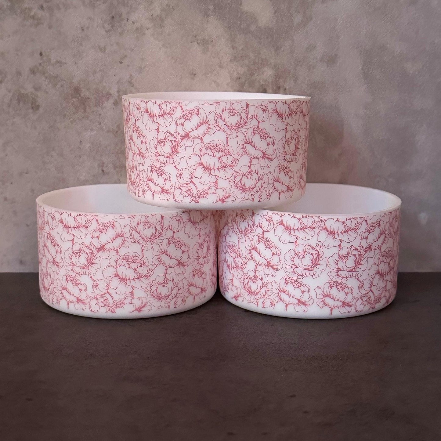 May include: Three white ceramic bowls with a pink floral pattern stacked on top of each other